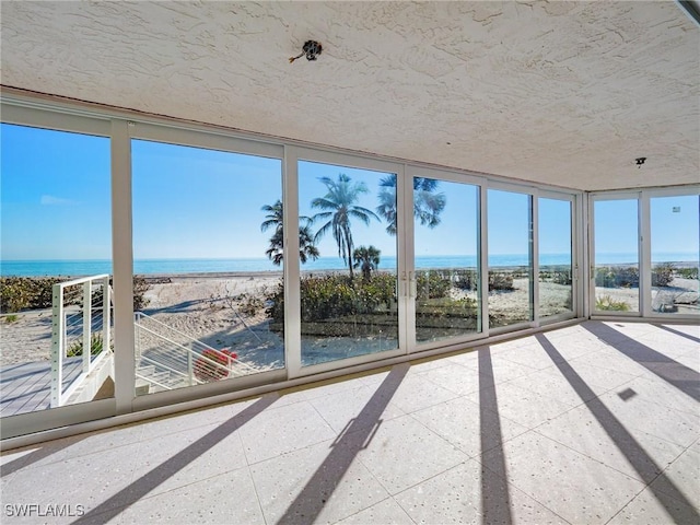 unfurnished sunroom featuring a view of the beach and a water view