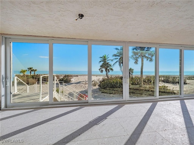 unfurnished sunroom featuring a water view, a healthy amount of sunlight, and a beach view