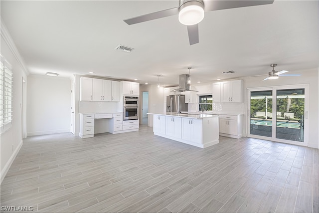 kitchen with pendant lighting, ceiling fan, island exhaust hood, appliances with stainless steel finishes, and white cabinetry