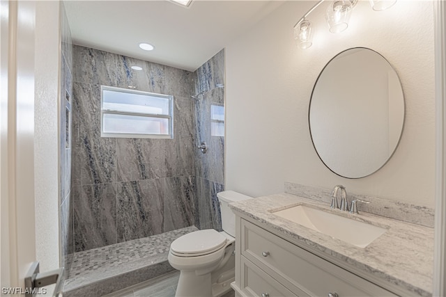 bathroom with toilet, a tile shower, and vanity