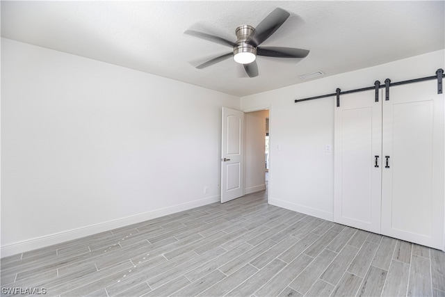 unfurnished bedroom featuring a barn door, light hardwood / wood-style floors, a closet, and ceiling fan