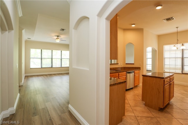 kitchen featuring dishwasher, light tile flooring, decorative light fixtures, ceiling fan with notable chandelier, and a center island