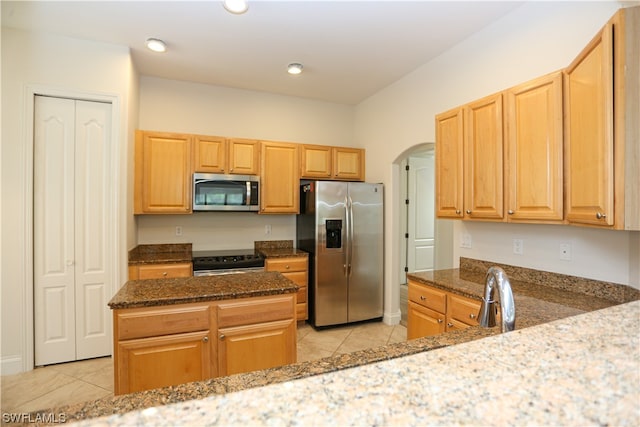 kitchen featuring kitchen peninsula, stainless steel appliances, light tile floors, and dark stone counters