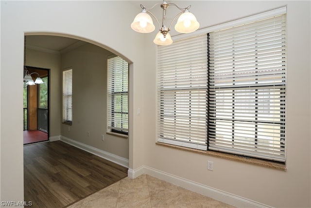 empty room featuring light tile floors, a notable chandelier, and ornamental molding