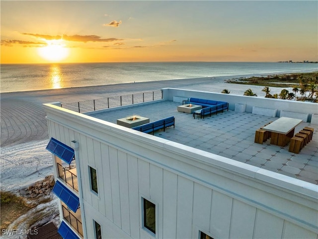 patio terrace at dusk with a water view, a view of the beach, and a fire pit