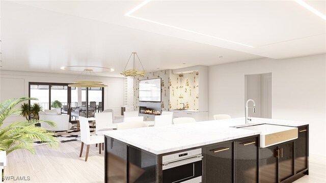 kitchen with sink, hanging light fixtures, a kitchen island with sink, oven, and light hardwood / wood-style floors