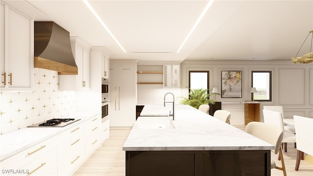 kitchen featuring stainless steel appliances, an island with sink, white cabinets, and wall chimney exhaust hood