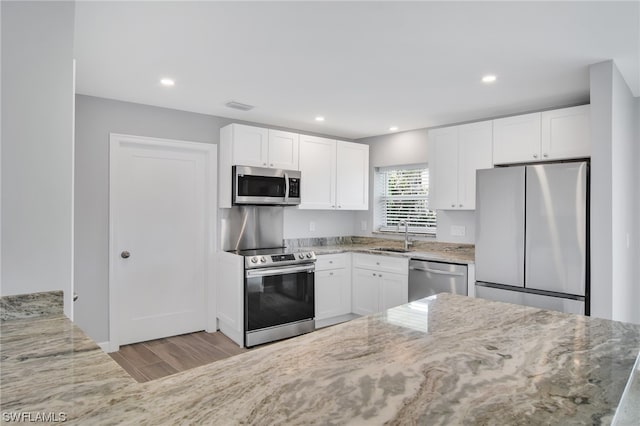 kitchen with white cabinets, appliances with stainless steel finishes, light stone counters, and sink