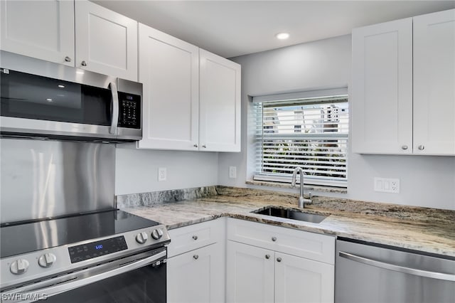 kitchen with white cabinets, stainless steel appliances, light stone counters, and sink