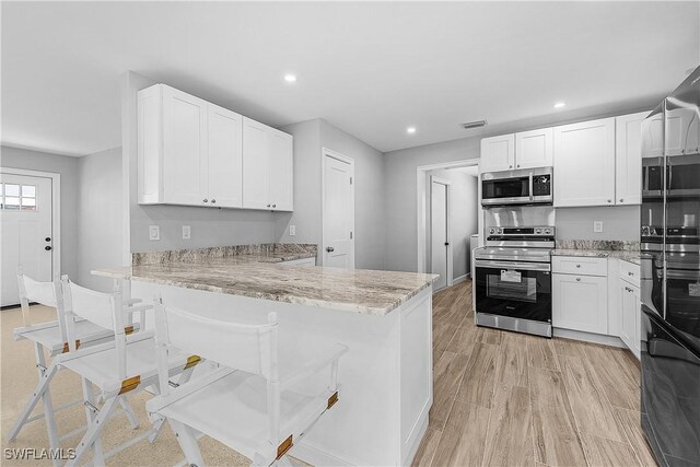 2 Fairview Blvd, Fort Myers Beach, FL 33931 - kitchen featuring appliances with stainless steel finishes, light stone countertops, white cabinetry, recessed lighting, and a kitchen breakfast bar