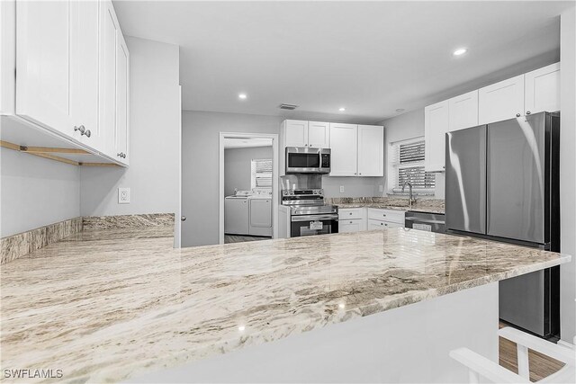 2 Fairview Blvd, Fort Myers Beach, FL 33931 - kitchen with stainless steel appliances, washer and clothes dryer, a sink, light stone countertops, and white cabinetry