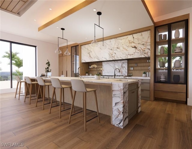 kitchen with open shelves, a kitchen breakfast bar, a large island with sink, and wood finished floors