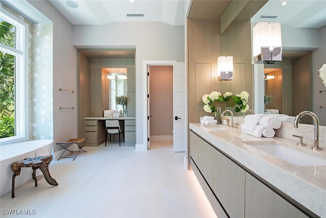 full bath featuring visible vents, double vanity, a freestanding tub, and a sink