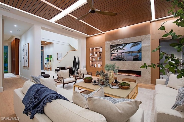 living room with built in features, recessed lighting, wood finished floors, ceiling fan, and a high end fireplace