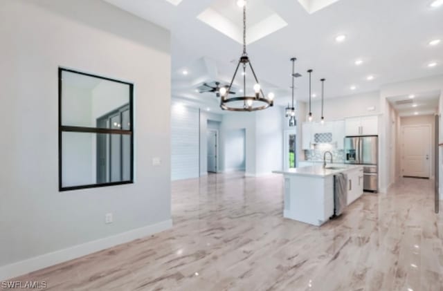 kitchen with coffered ceiling, white cabinetry, hanging light fixtures, an inviting chandelier, and a center island with sink