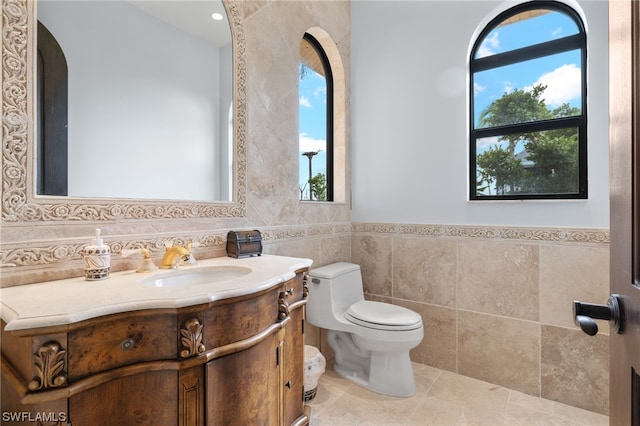 bathroom with tile walls, toilet, vanity, and tile flooring