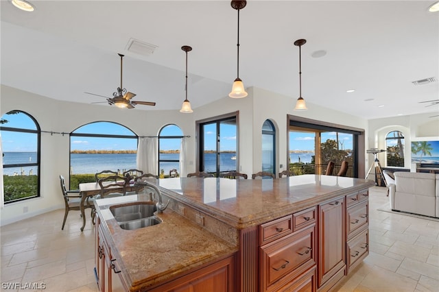 kitchen featuring light stone countertops, a water view, and an island with sink