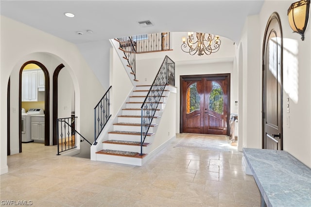 tiled entryway with a high ceiling, a notable chandelier, and separate washer and dryer