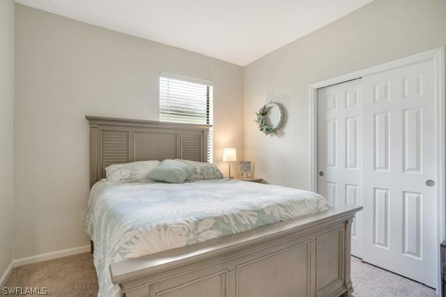 bedroom with baseboards, a closet, and light colored carpet