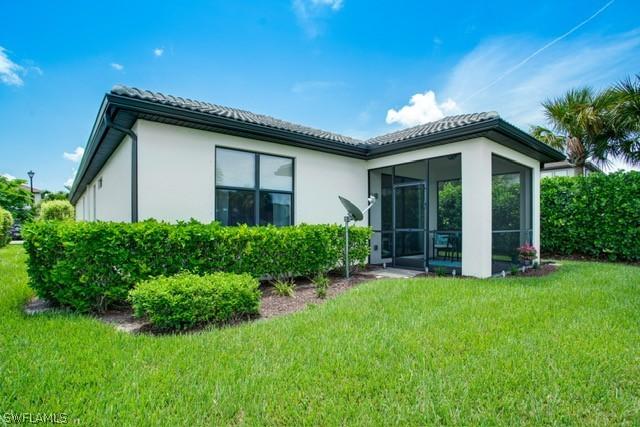 rear view of property featuring a sunroom, a tile roof, and a yard