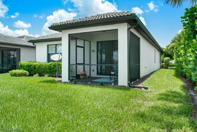 back of property with a sunroom, a tile roof, stucco siding, and a yard