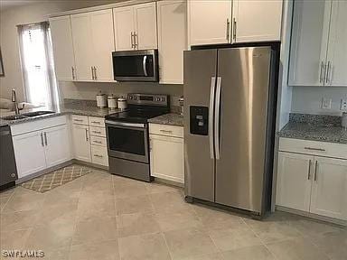 kitchen featuring appliances with stainless steel finishes, dark stone counters, white cabinets, and a sink