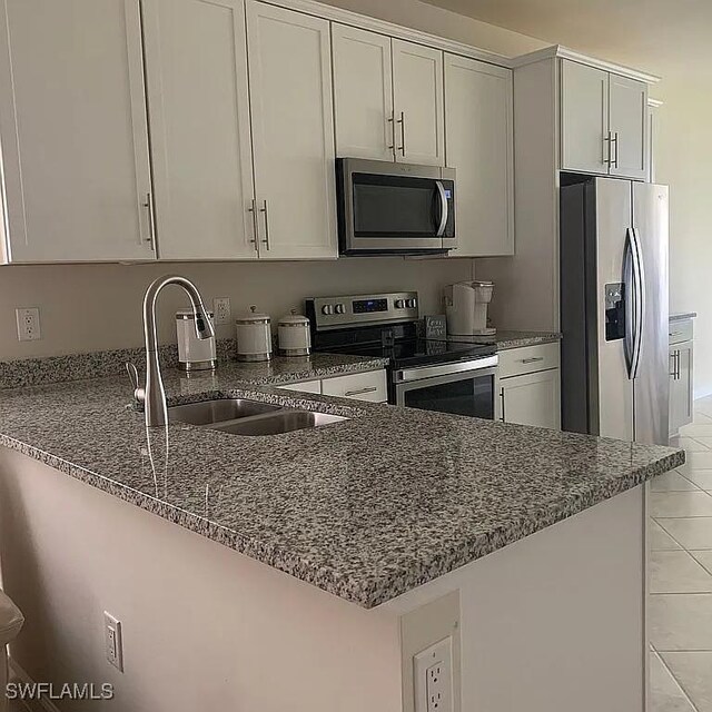 kitchen featuring dark stone counters, appliances with stainless steel finishes, a peninsula, white cabinetry, and a sink