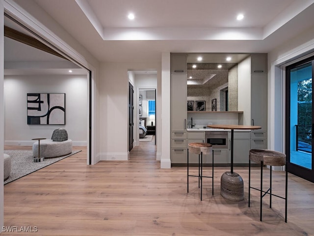 kitchen with gray cabinets, a tray ceiling, a breakfast bar area, and light hardwood / wood-style flooring