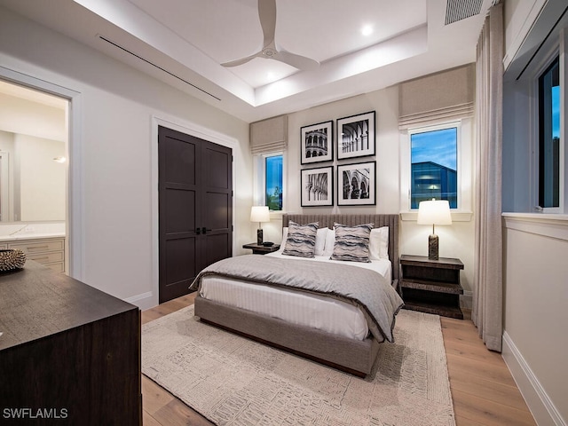 bedroom with a tray ceiling, ceiling fan, and light hardwood / wood-style flooring