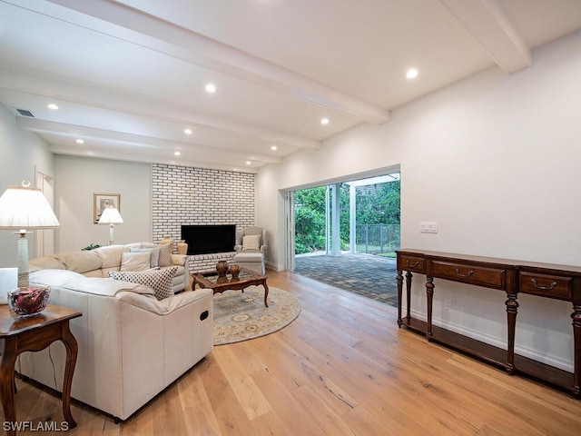 living room featuring beam ceiling, light wood-type flooring, and a brick fireplace