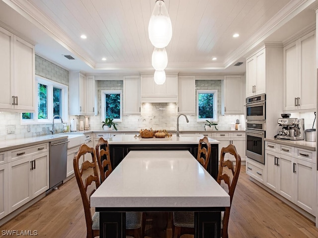 kitchen with light wood-type flooring, decorative light fixtures, a kitchen island, and a tray ceiling