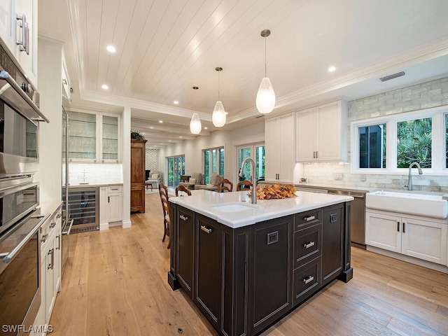 kitchen with sink, beverage cooler, pendant lighting, and a center island with sink