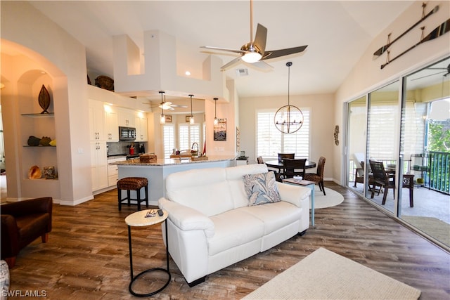 living room with built in features, high vaulted ceiling, dark wood-type flooring, and ceiling fan with notable chandelier