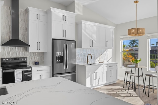 kitchen with white cabinetry, wall chimney exhaust hood, hanging light fixtures, stainless steel appliances, and light stone counters