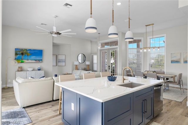 kitchen with light stone counters, a kitchen island with sink, sink, decorative light fixtures, and light hardwood / wood-style flooring