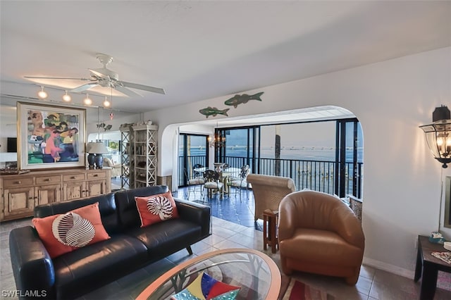 living room with light tile flooring, a water view, track lighting, and ceiling fan with notable chandelier