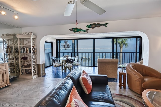 tiled living room with rail lighting, a water view, and ceiling fan with notable chandelier