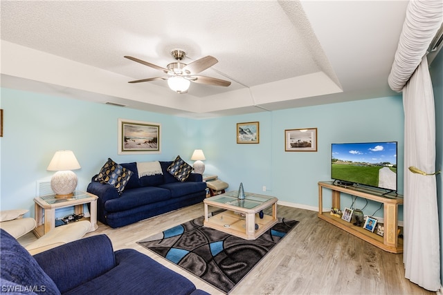 living room with a tray ceiling, light hardwood / wood-style floors, ceiling fan, and a textured ceiling