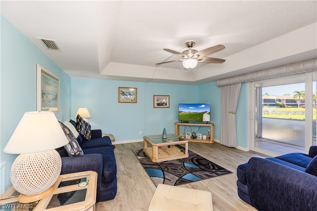 living room featuring a raised ceiling, ceiling fan, a textured ceiling, and light wood-type flooring