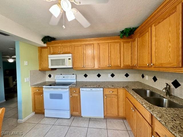 kitchen featuring sink, white appliances, light tile patterned floors, ceiling fan, and stone counters