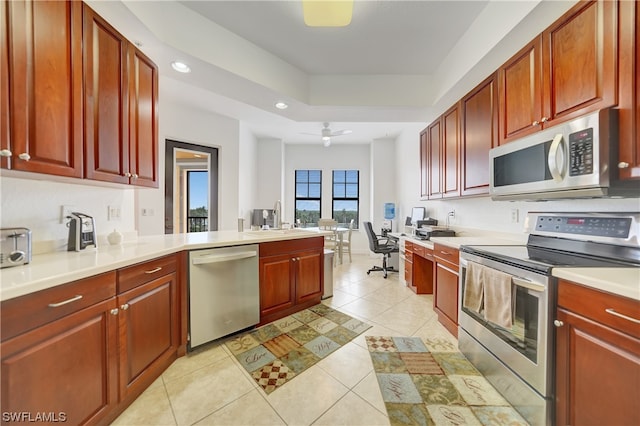 kitchen featuring light tile patterned flooring, sink, appliances with stainless steel finishes, a tray ceiling, and ceiling fan