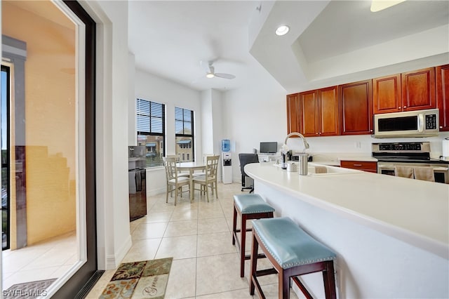 kitchen with a kitchen bar, sink, light tile patterned floors, appliances with stainless steel finishes, and ceiling fan