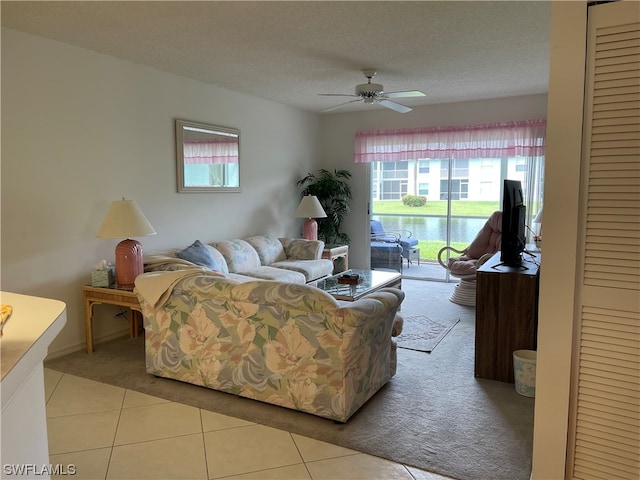 living room with a water view, ceiling fan, a textured ceiling, and light tile flooring