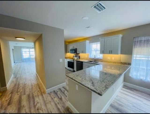 kitchen featuring sink, stainless steel appliances, light stone counters, light hardwood / wood-style floors, and kitchen peninsula