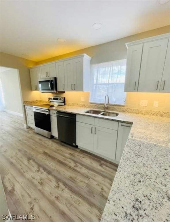 kitchen featuring light stone counters, appliances with stainless steel finishes, light hardwood / wood-style floors, and sink