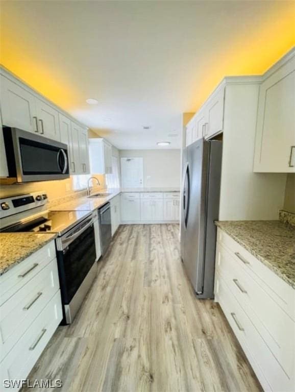 kitchen featuring appliances with stainless steel finishes, sink, white cabinets, light stone counters, and light hardwood / wood-style floors