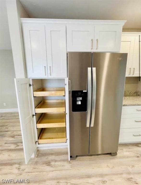 kitchen with stainless steel refrigerator with ice dispenser, white cabinetry, light stone counters, and light hardwood / wood-style flooring