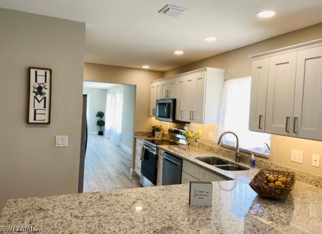 kitchen featuring sink, light hardwood / wood-style flooring, white cabinetry, stainless steel appliances, and light stone counters