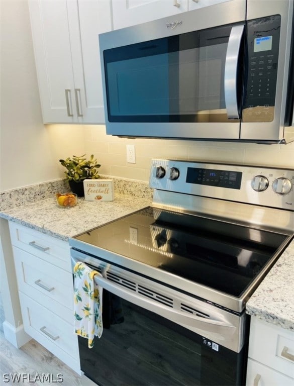 kitchen featuring stainless steel appliances, white cabinetry, backsplash, and light stone counters