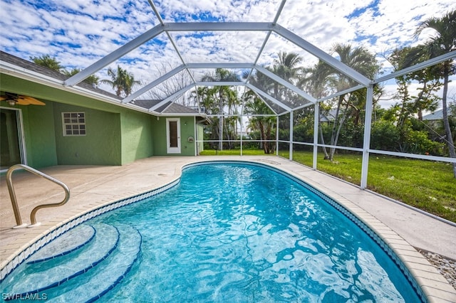 view of swimming pool featuring a yard, glass enclosure, ceiling fan, and a patio